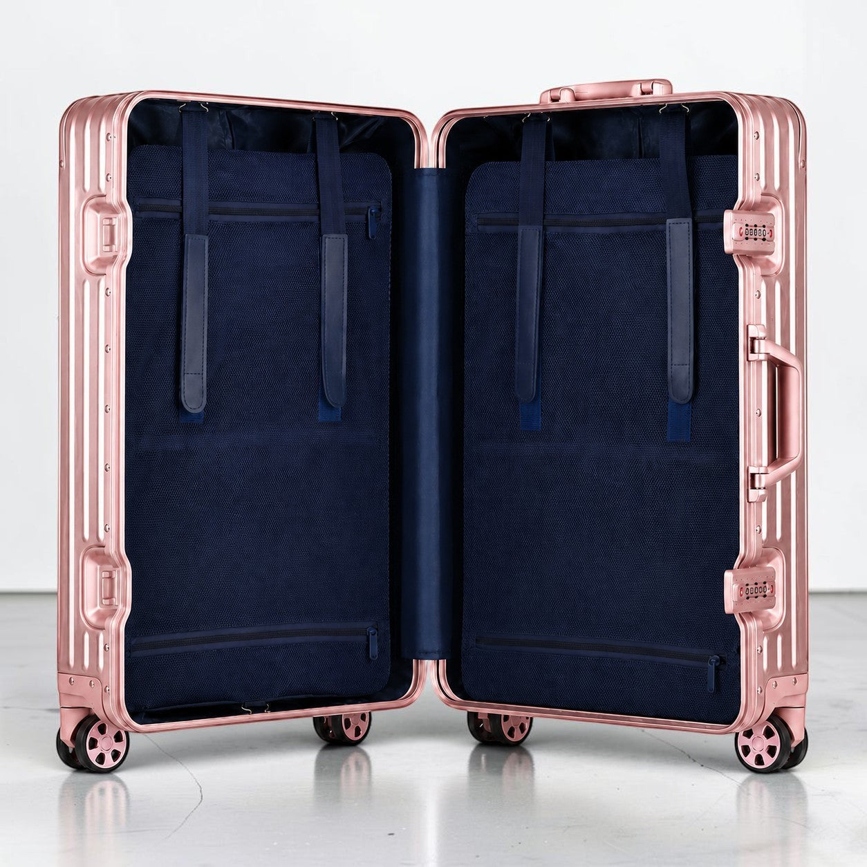 CASE.01 aluminum suitcase in rose gold with navy blue interior, featuring straps and zippered compartments. Smooth rolling wheels.